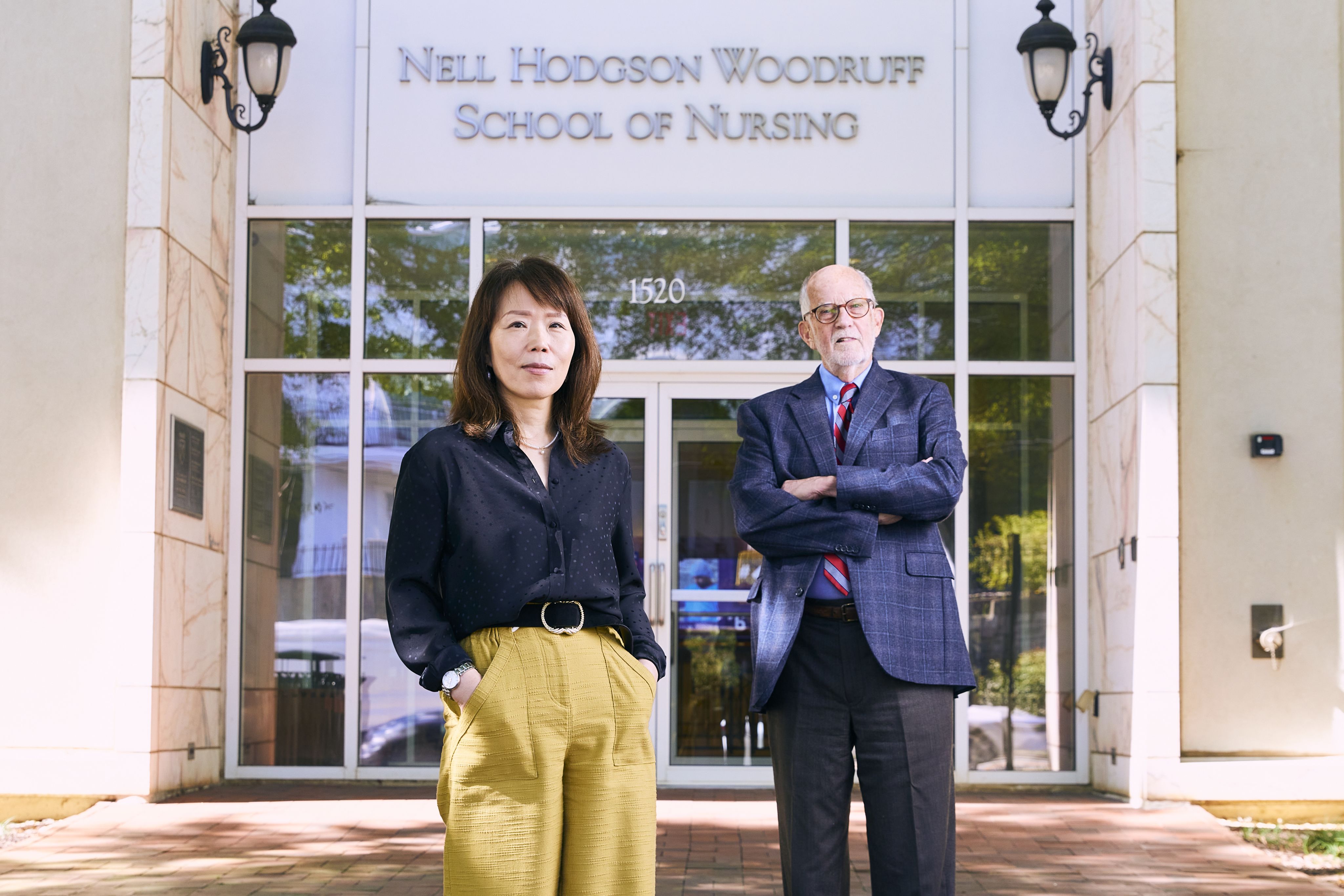 Two professors standing side by side in front of the School of Nursing