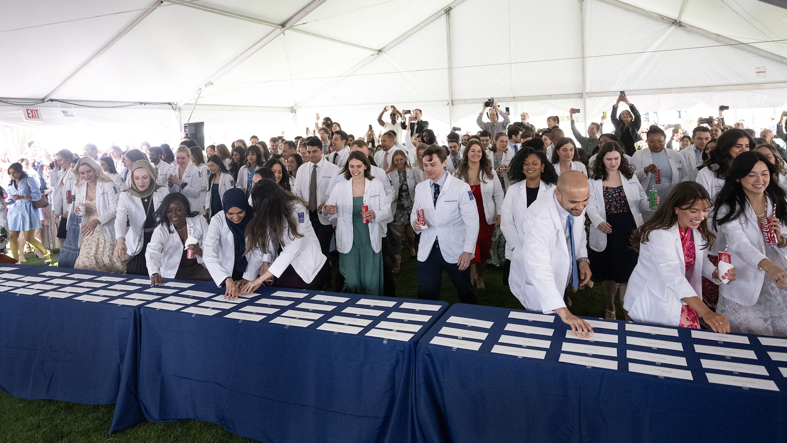 Students in white coats race forward to pick up white envelopes off a table