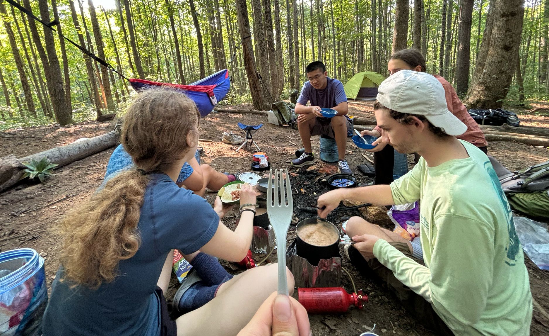 Photo of Outdoor Emory students on camping trip, sitting around a fire making breakfast.