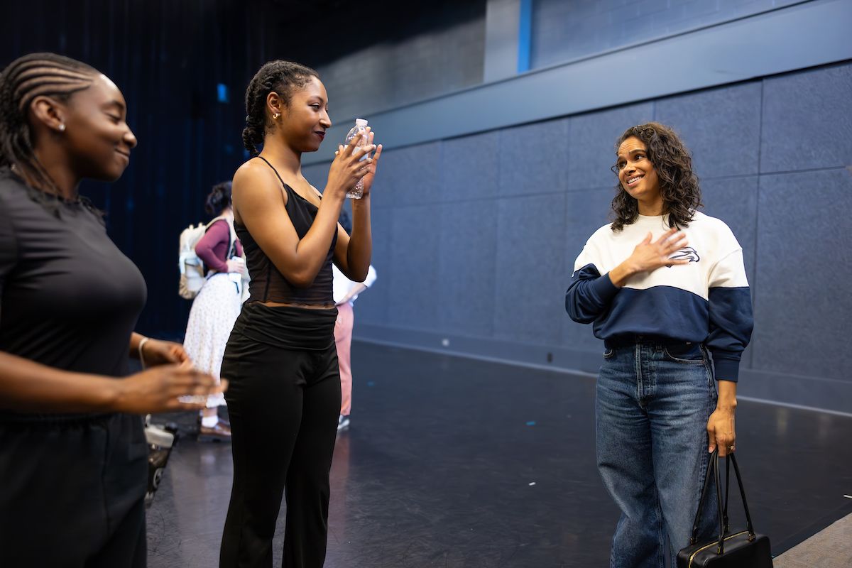 Two students smile at ballet dancer Misty Copeland, who stands with her hand on her heart.