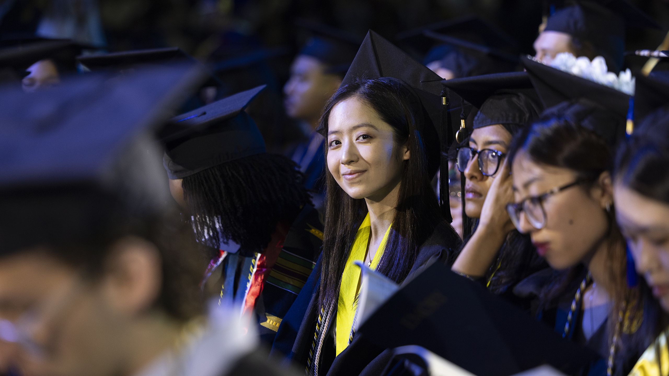 A graduate in cap and gown smiles in the crowd