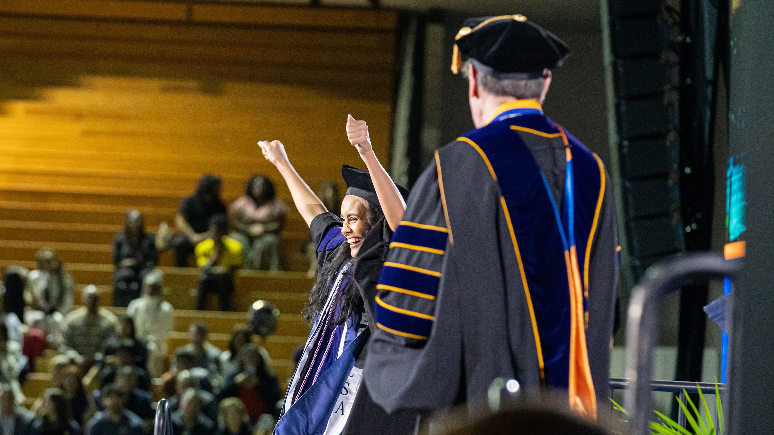 A graduate raises her arms in celebration after receiving her diploma
