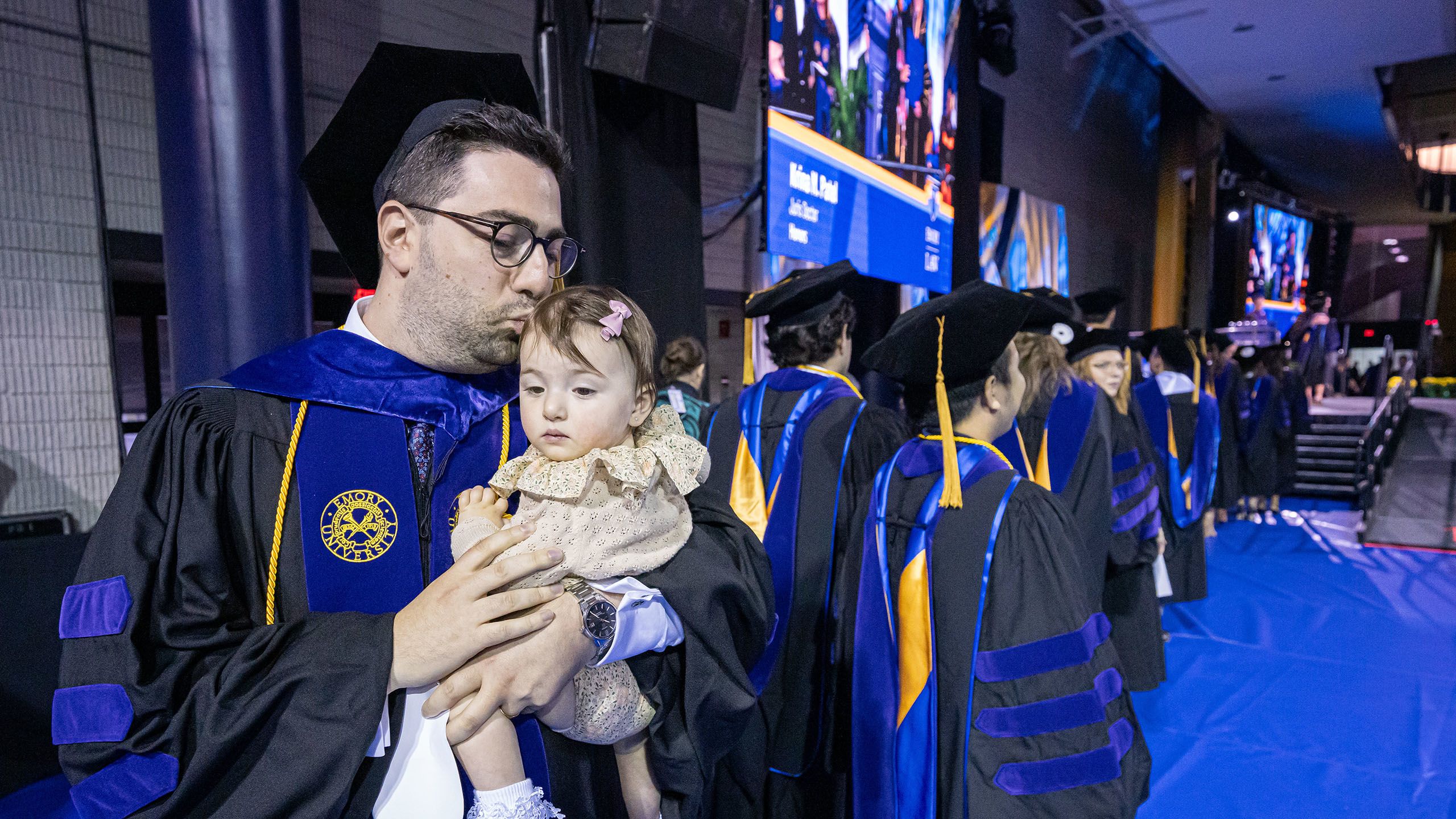 A graduate holds his baby while waiting to walk across the stage