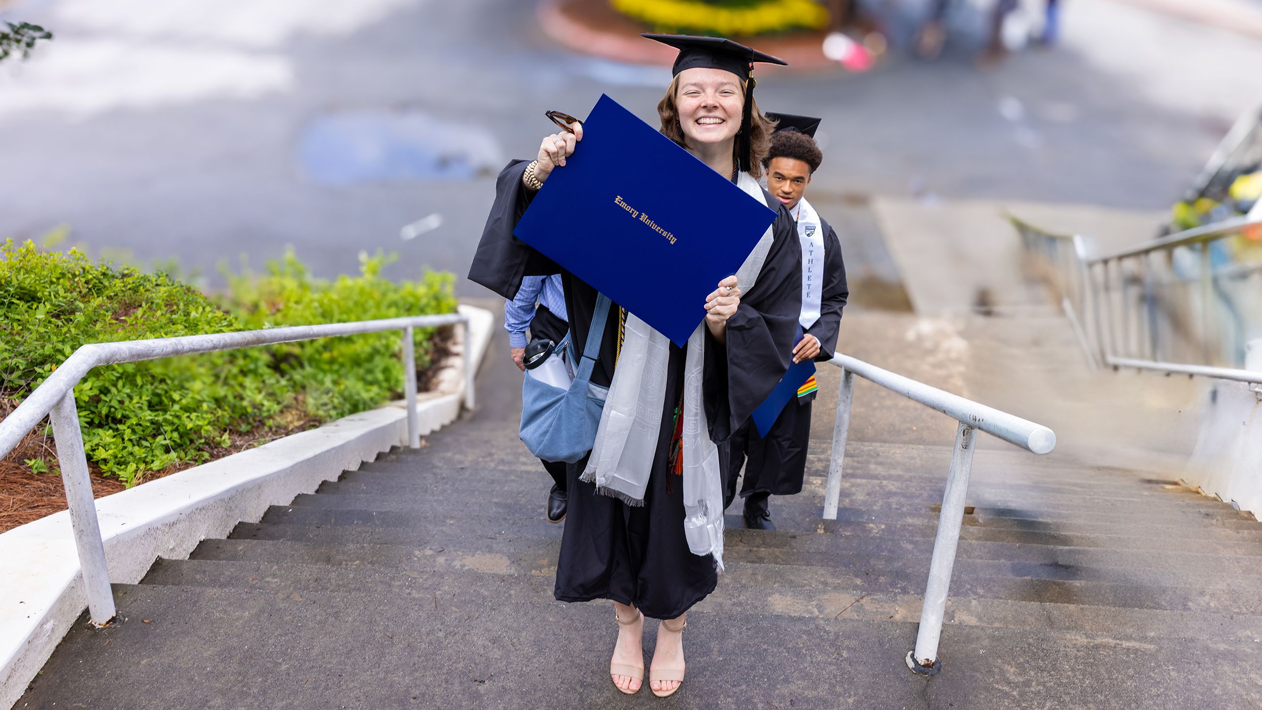 A grad holds up her degree while standing on the stairs