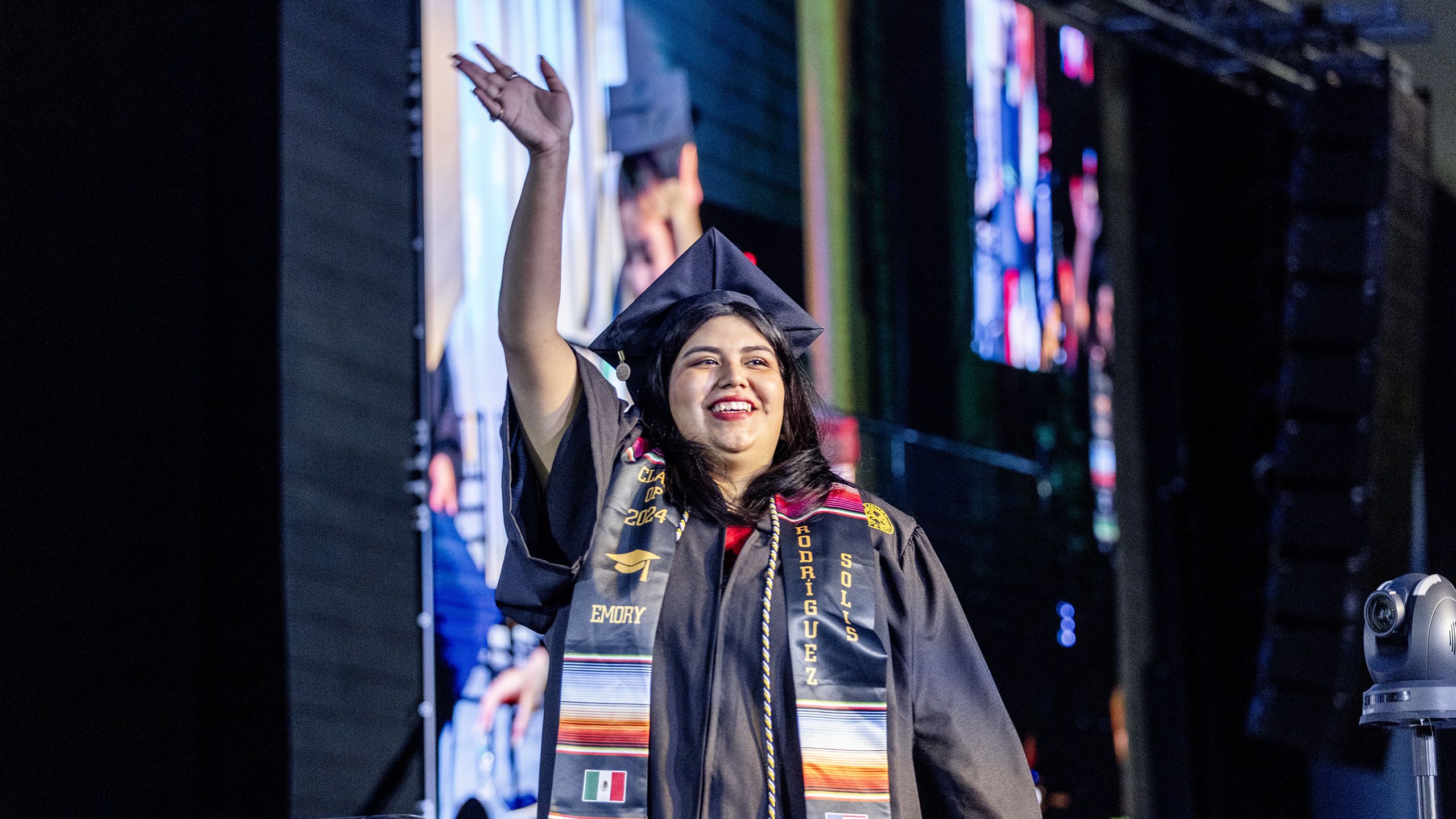 A graduate waves as she crosses the stage