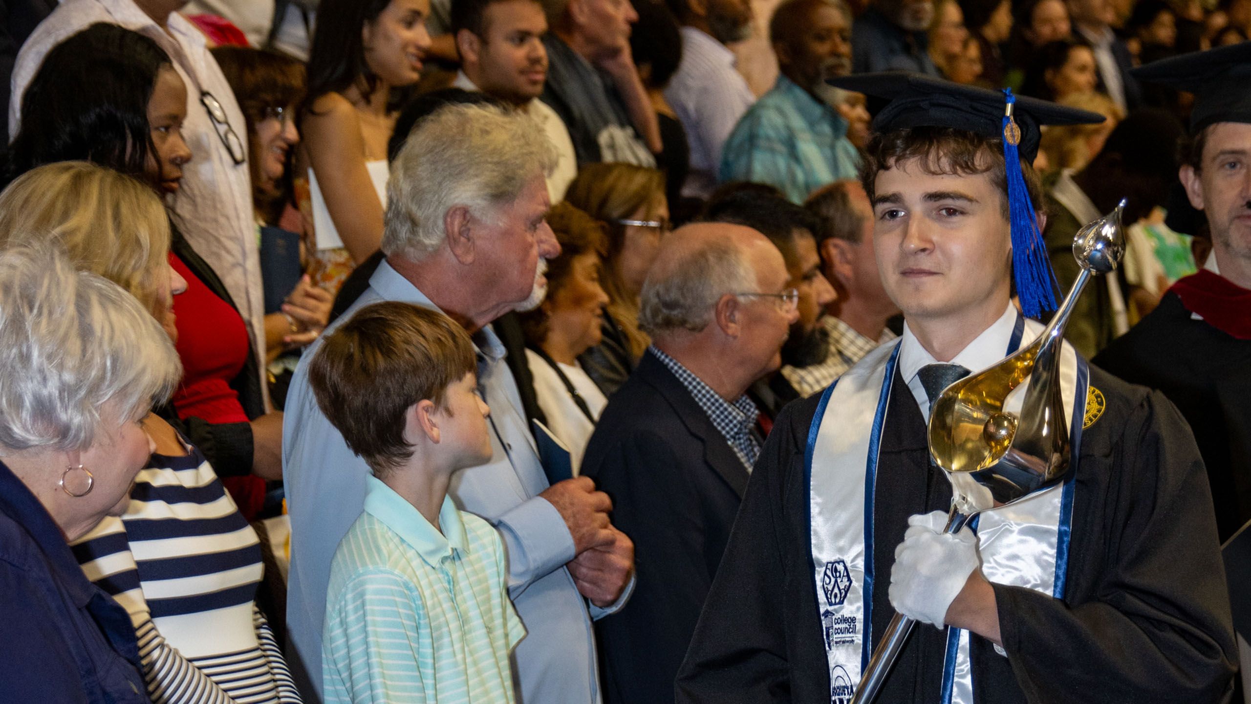 An Oxford student in cap and gown carries the ceremonial mace