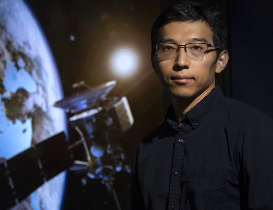 Xiao Wang stands before a projected image of a satellite