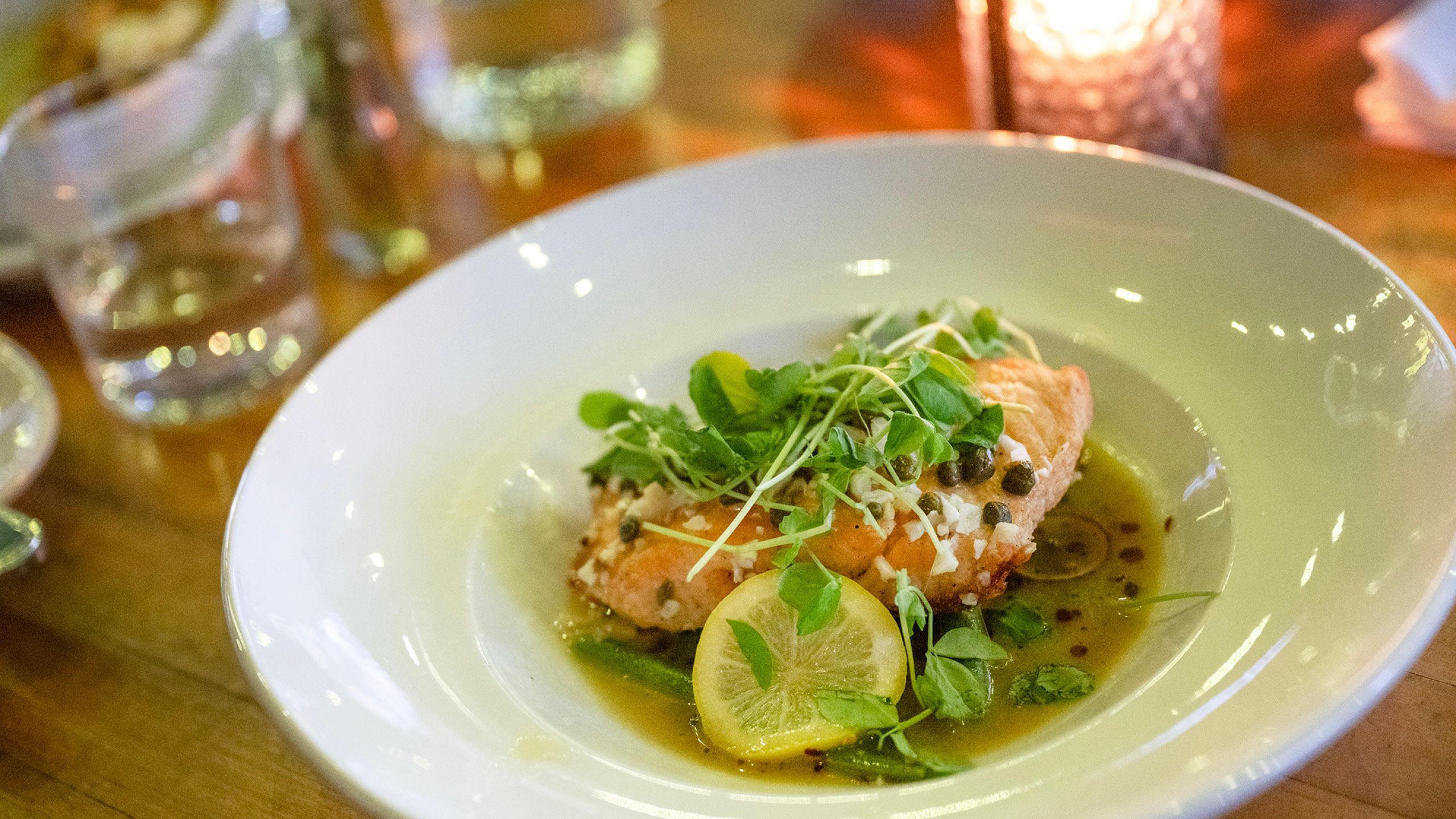 Food photo of salmon with herb and lemon toppings on a white plate.