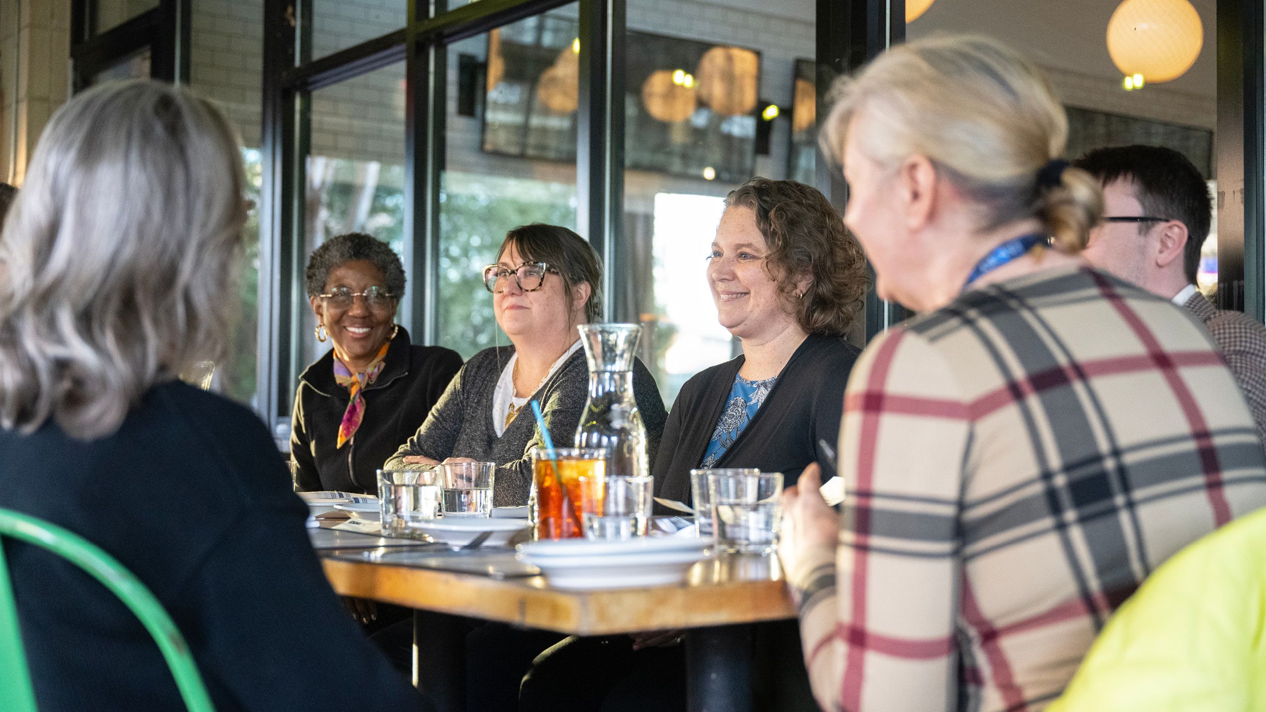 A group of people sitting at a restaurant table smiling as they talk to each other. 