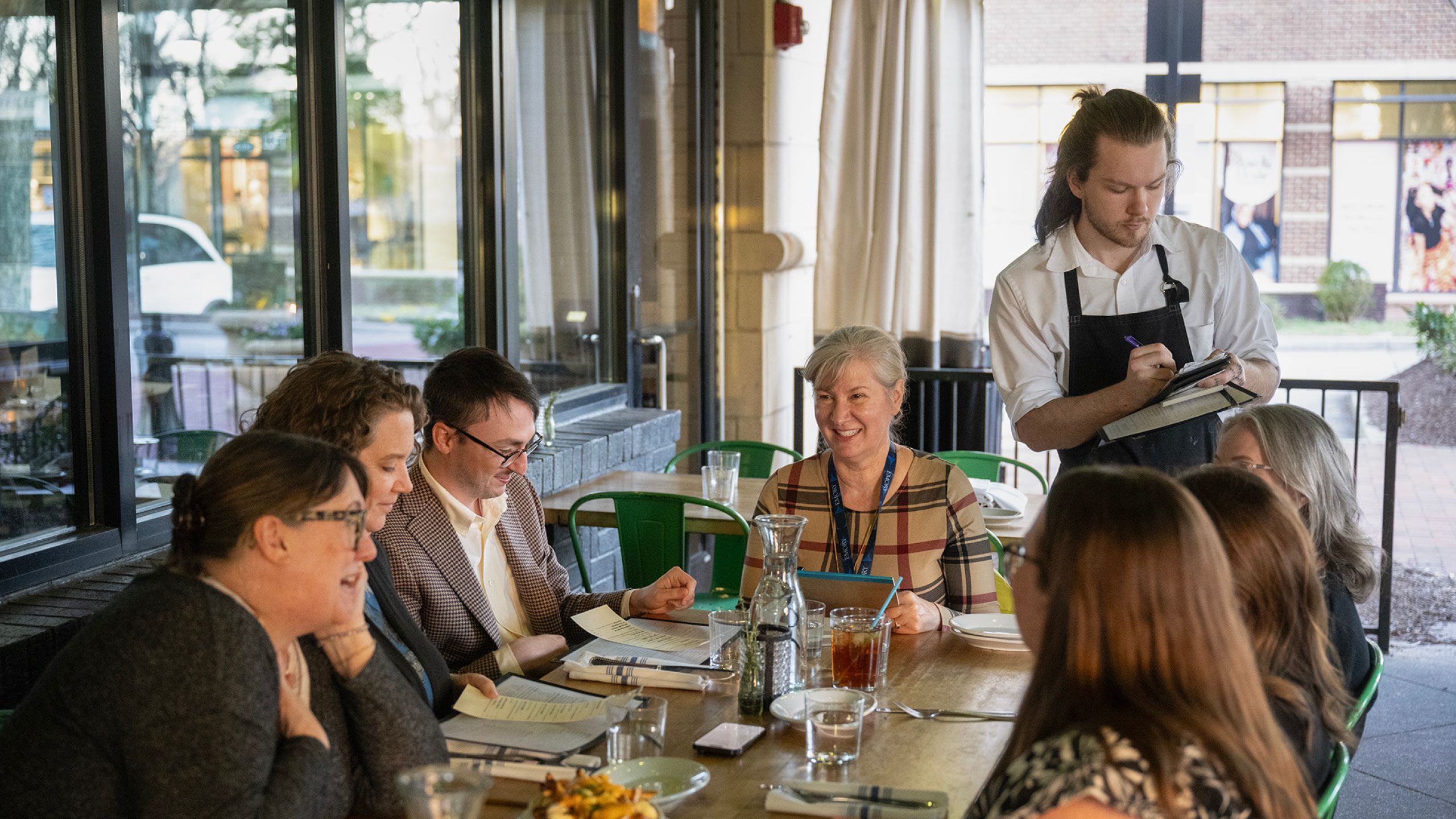 A waiter taking the order of a group of people sitting around a restaurant table. 
