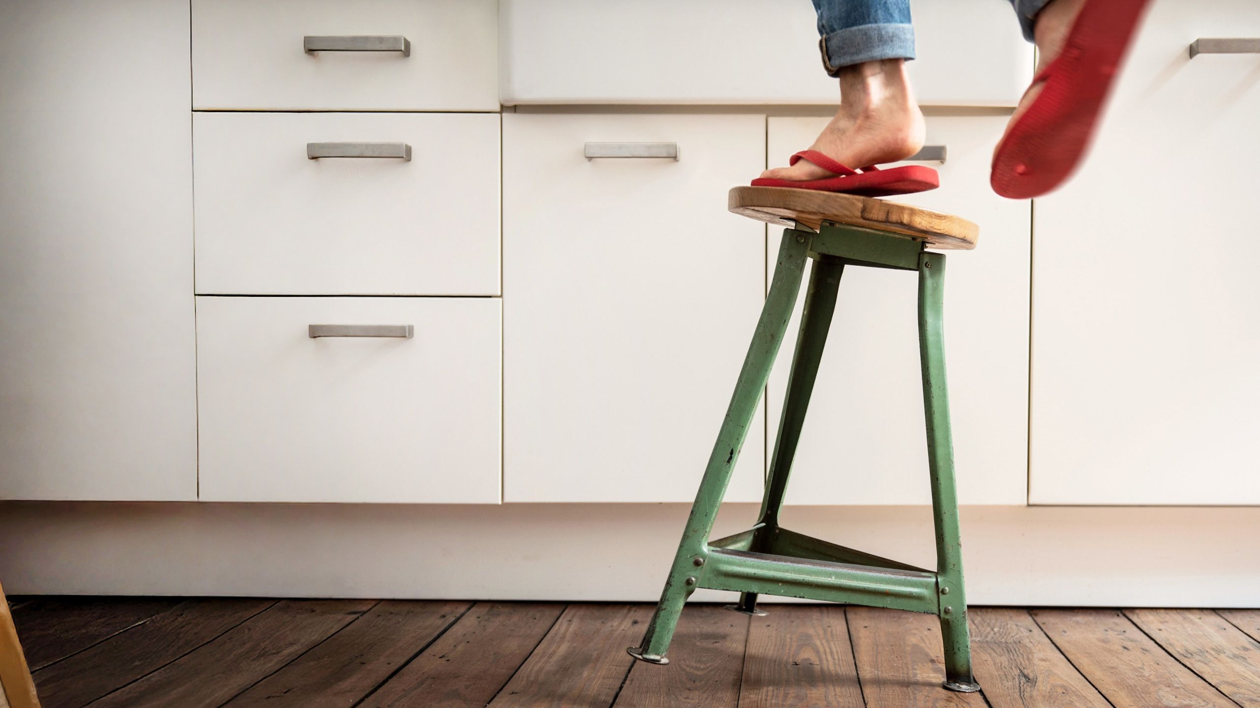 A photo illustration of a woman (you can only see her red flip-flop clad feet and the bottoms of her jeans) falling off a green stool