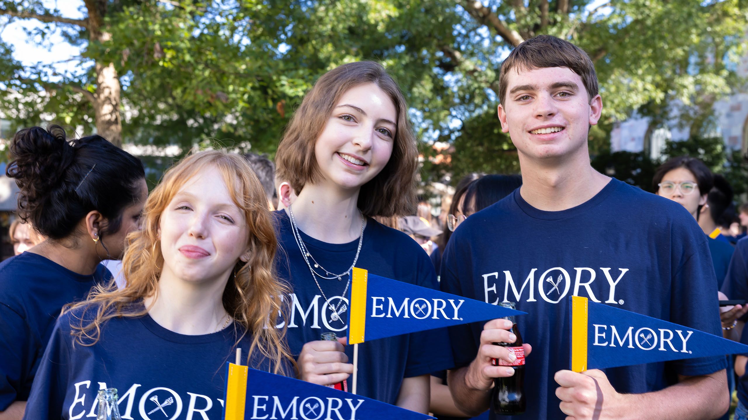 Three smiling students hold Emory pennants and bottles of Coca Cola