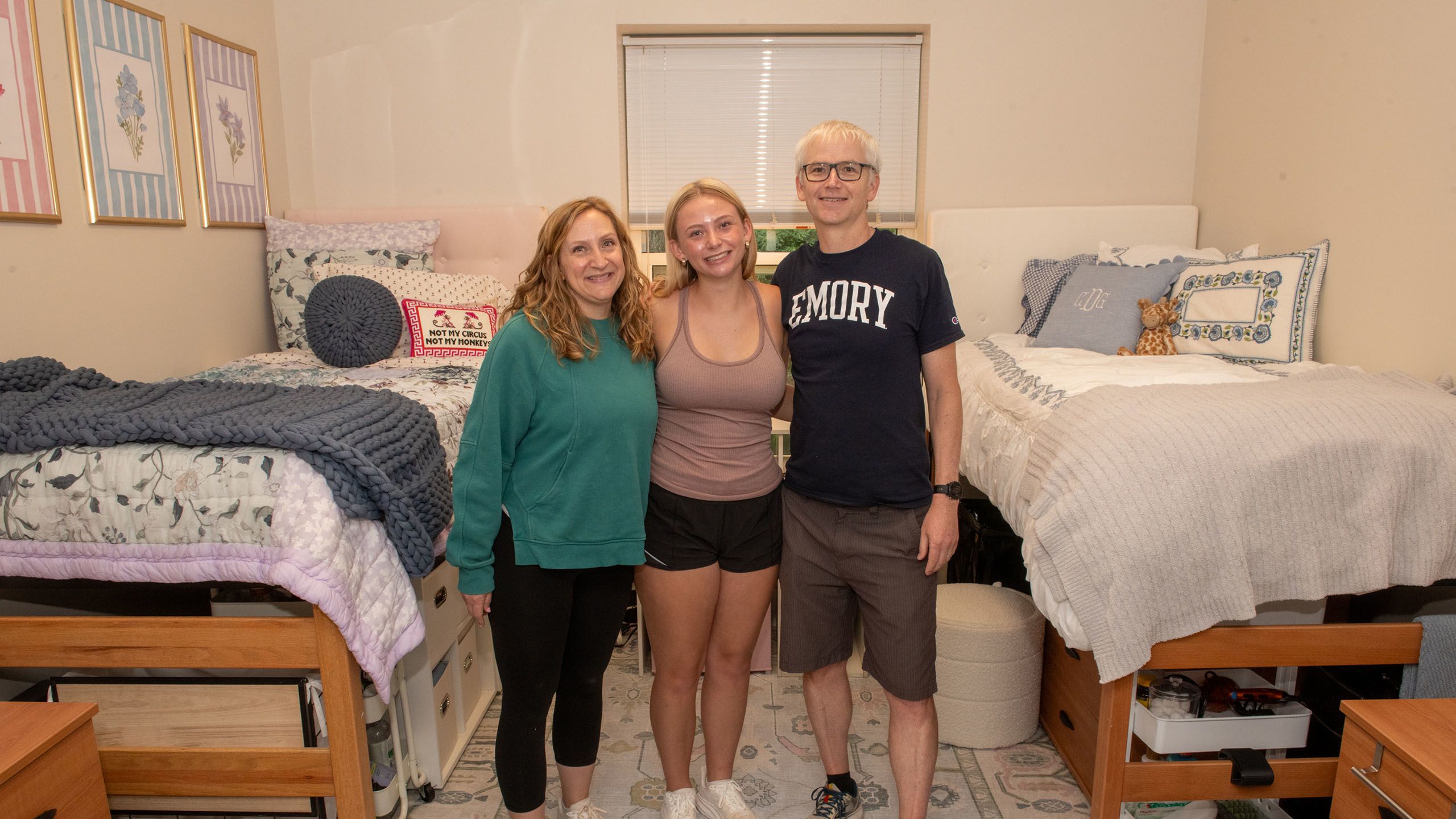 A female student, flanked by her parents, smiling in her new room
