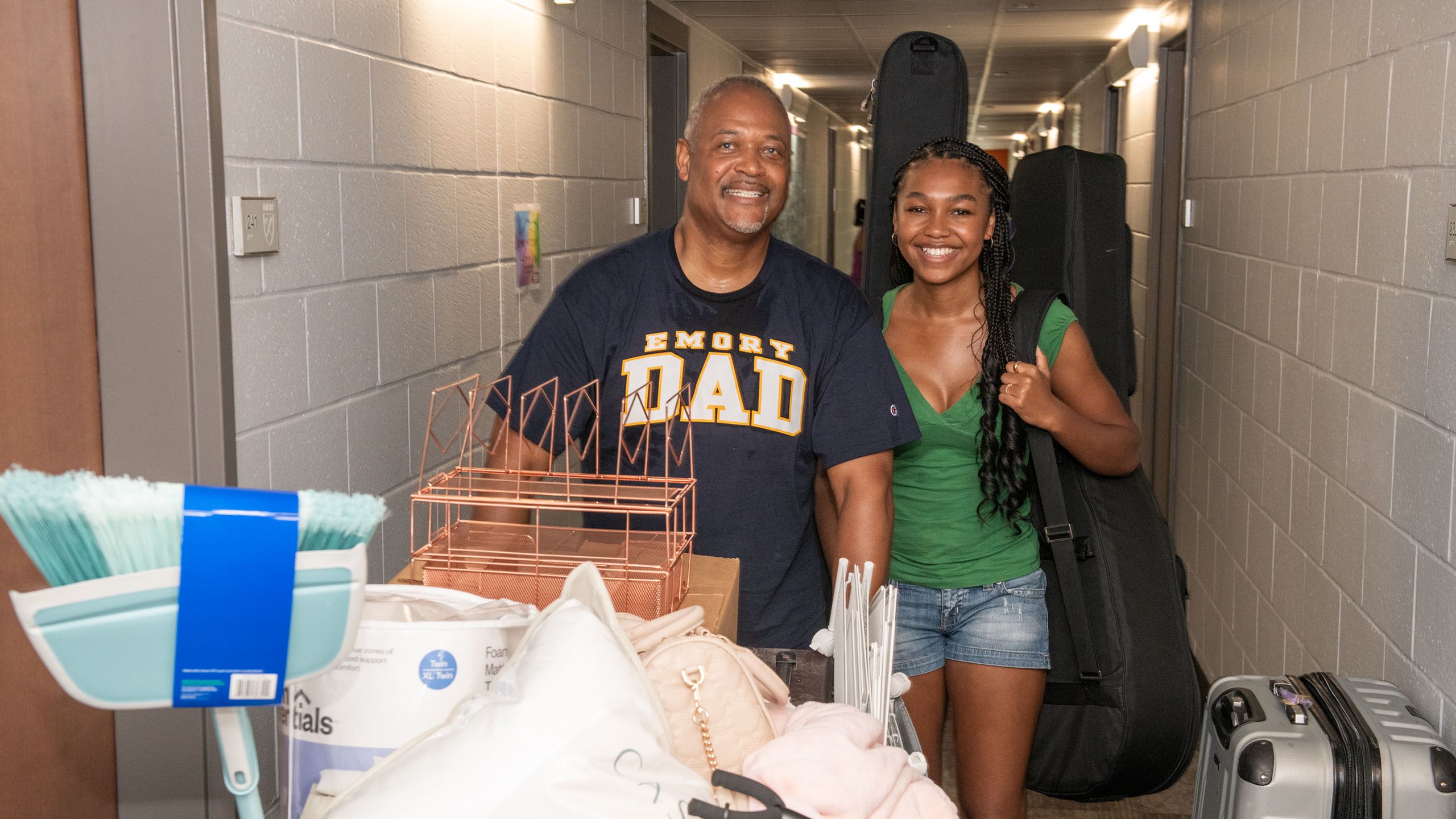 Incoming student walks down the residence hallway with her father, wearing an Emory Dad shirt and pushing a cart
