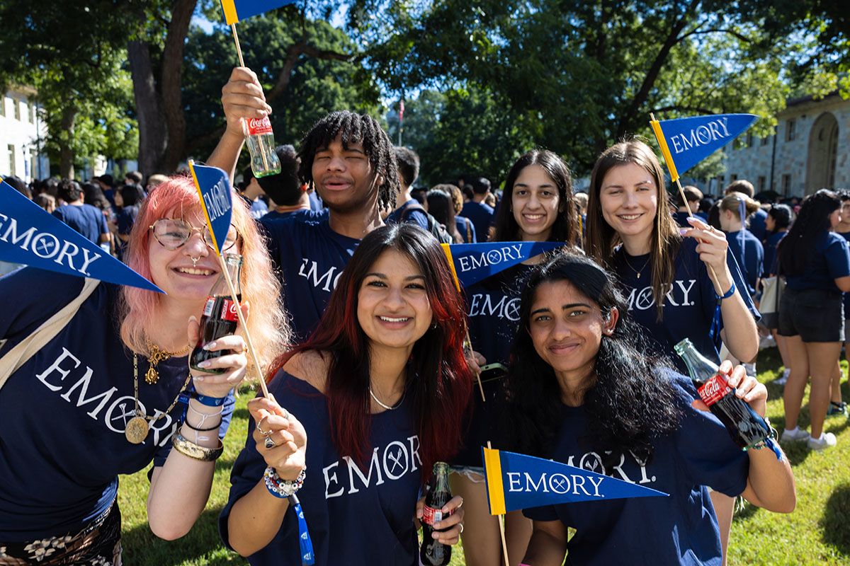 large group of students hold Coca Cola bottles and wave Emory pennants, smiling