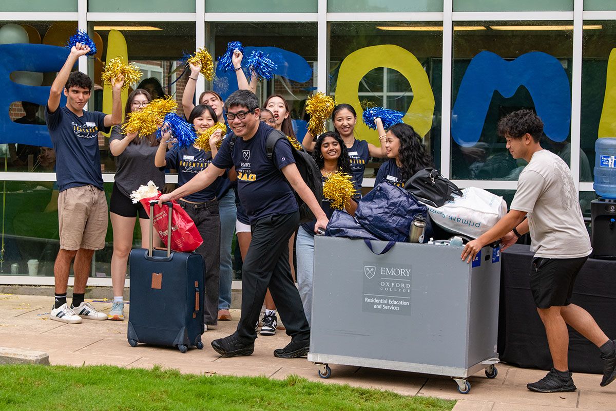 Orientation leaders wave pom poms and cheer as students steer large moving carts