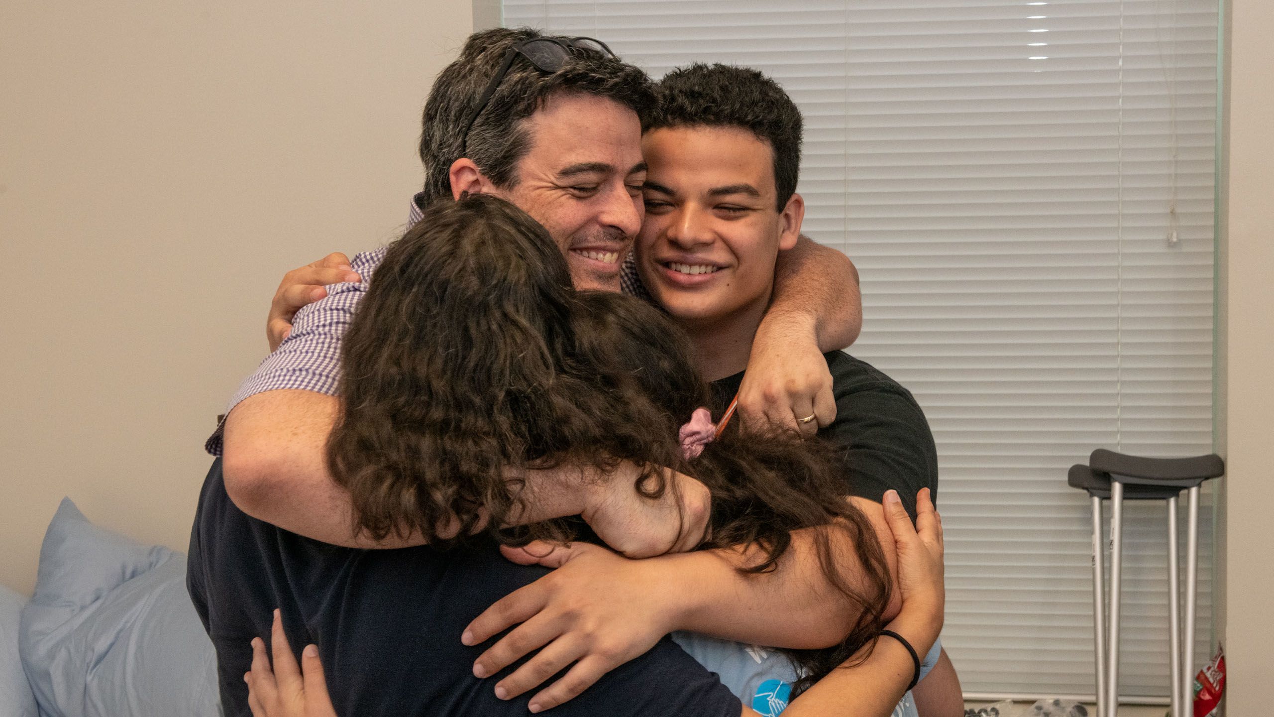A family of four hugging their child in their dorm room