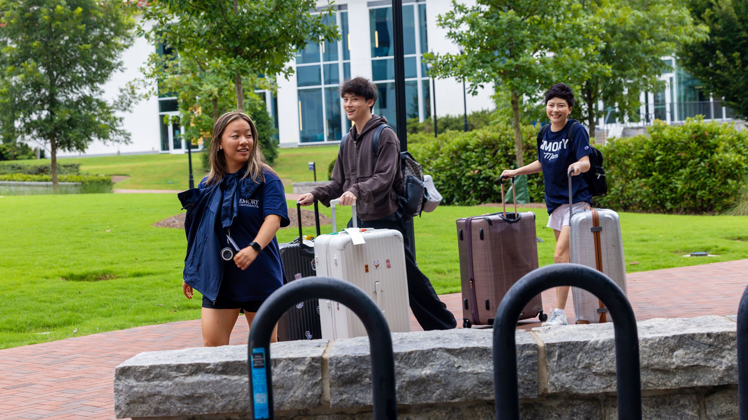 incoming students walk across campus, rolling large suitcases