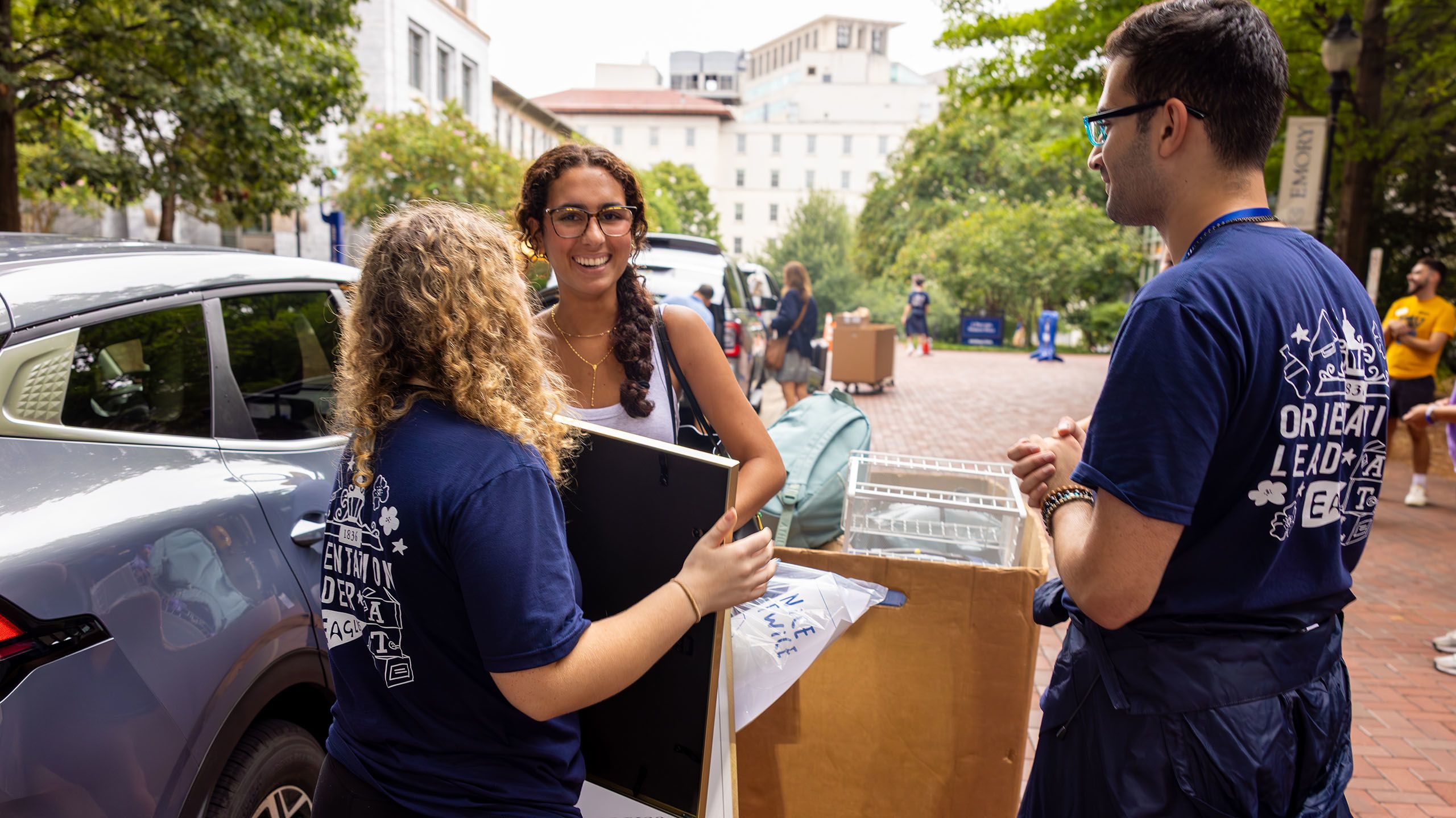 incoming student moves items from car, laughs with orientation leaders