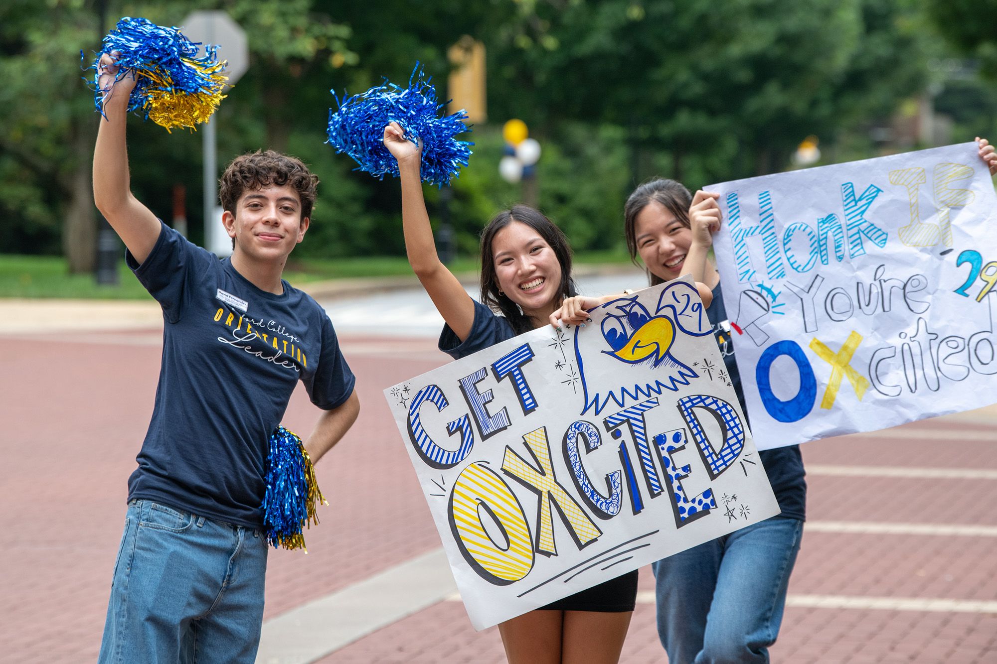 Three orientation leaders wave blue pom poms and hold signs that say Get Oxcited and Honk if you're Oxcited