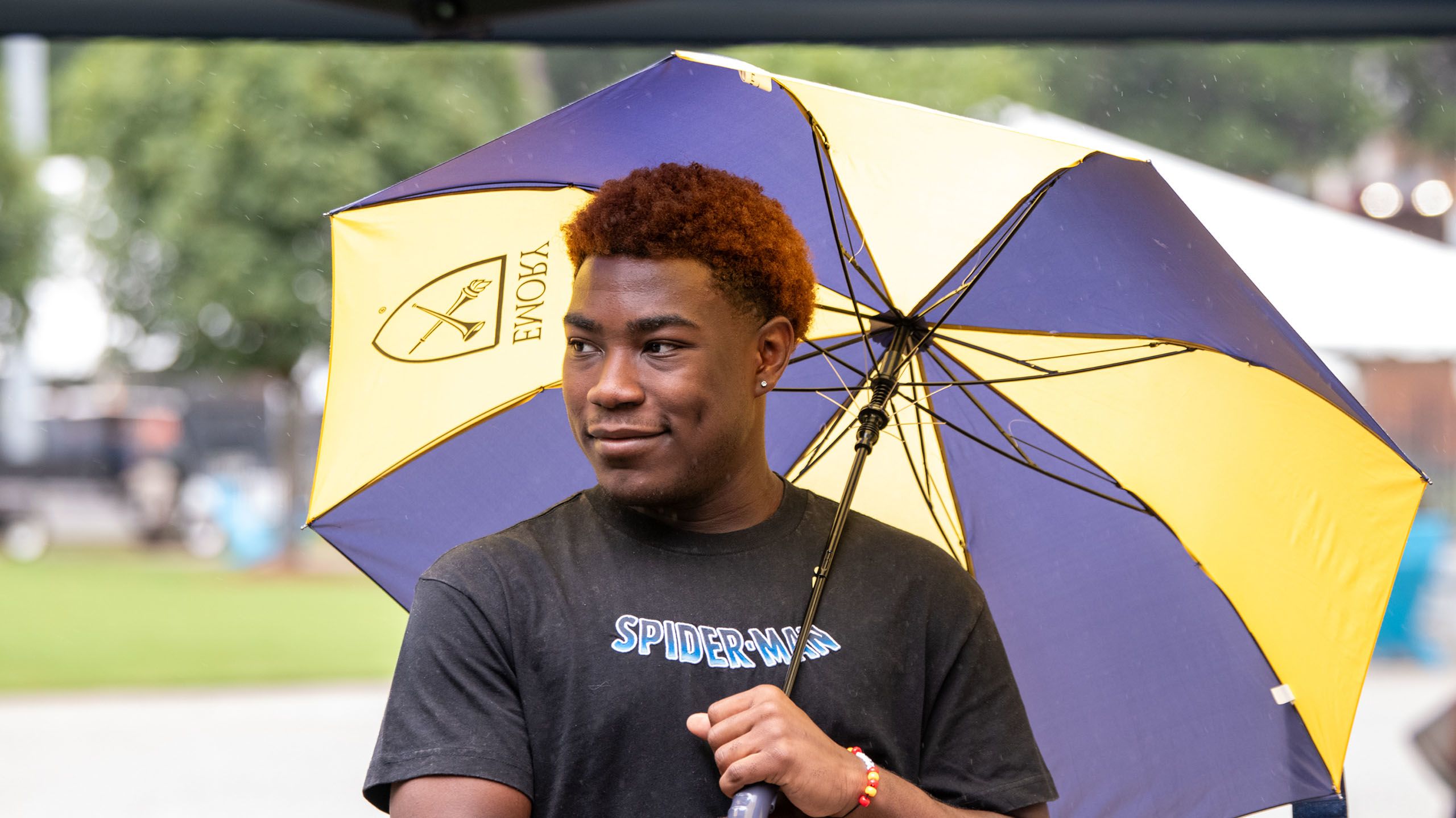 A student volunteer holds an umbrella and smiles to something off camera