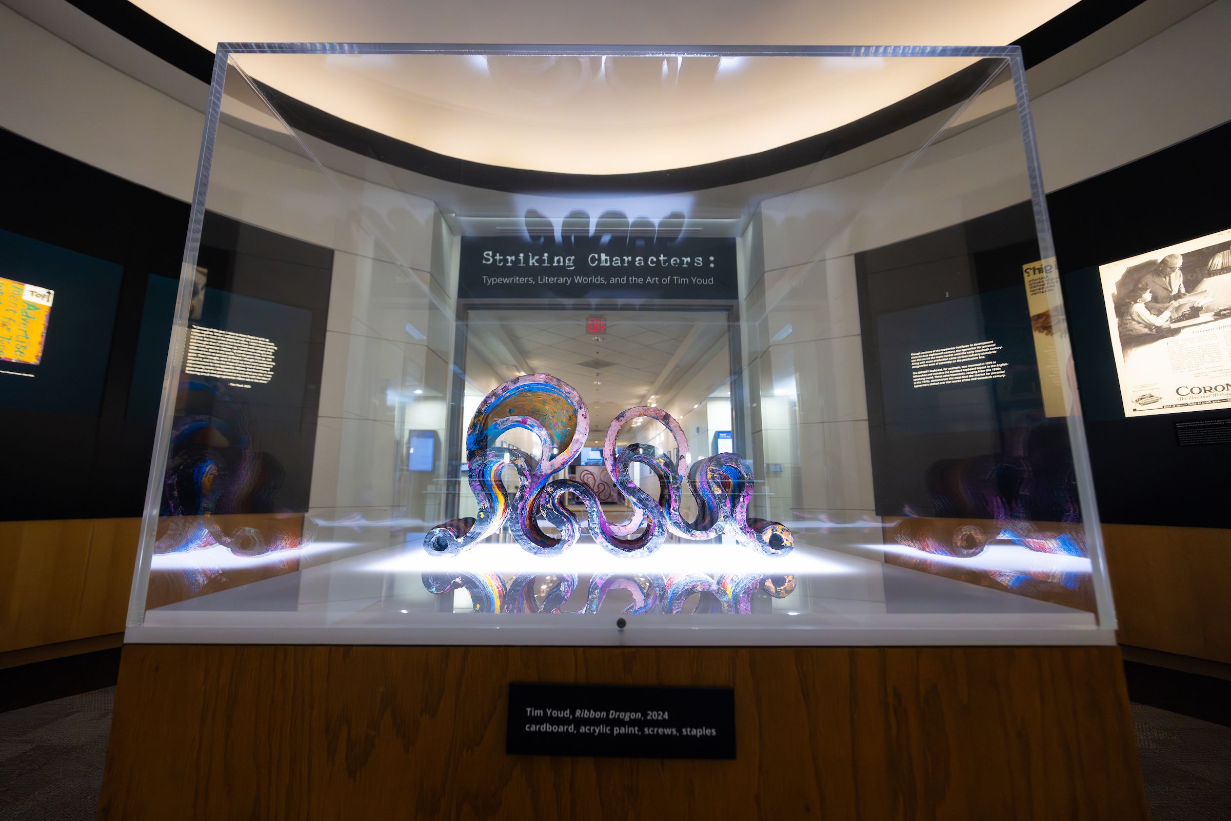 At the center of the photo, a purple and pink snakelike sculpture sits in a glass case. It is framed by a doorway, above which we see the words, "Striking Characters."
