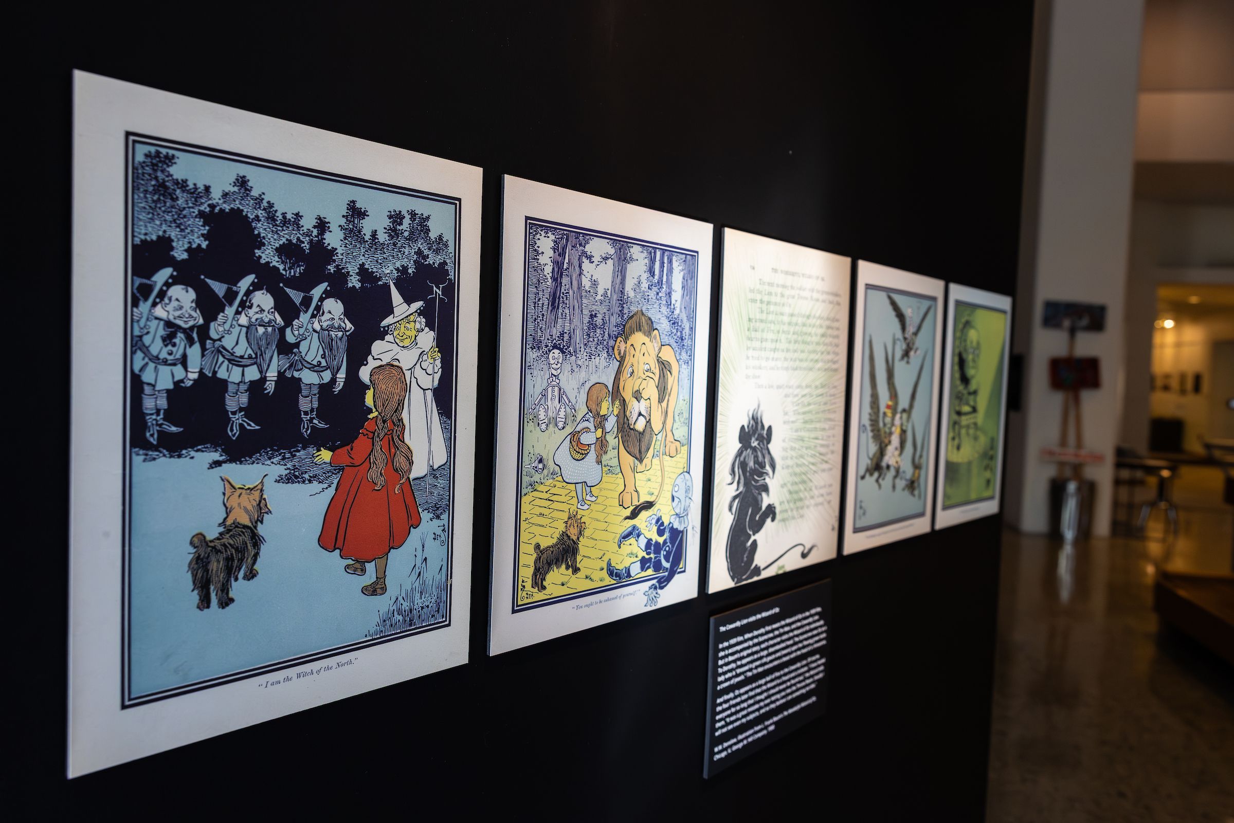 Prints of pages from "The Wonderful Wizard of Oz" by L. Frank Baum line a black wall.