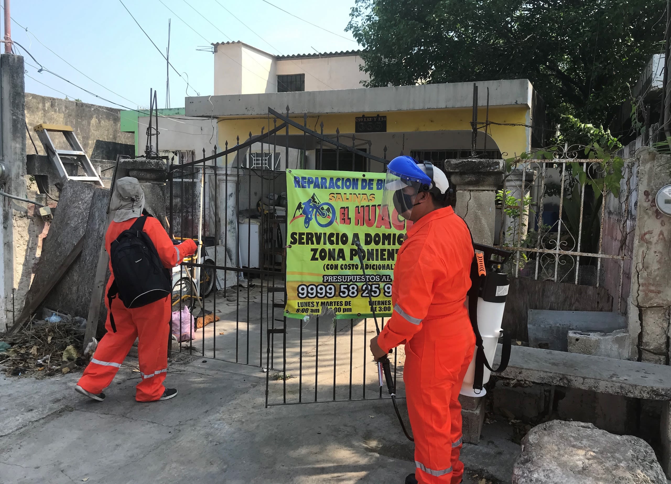People wearing protective gear spray an area for mosquitos.