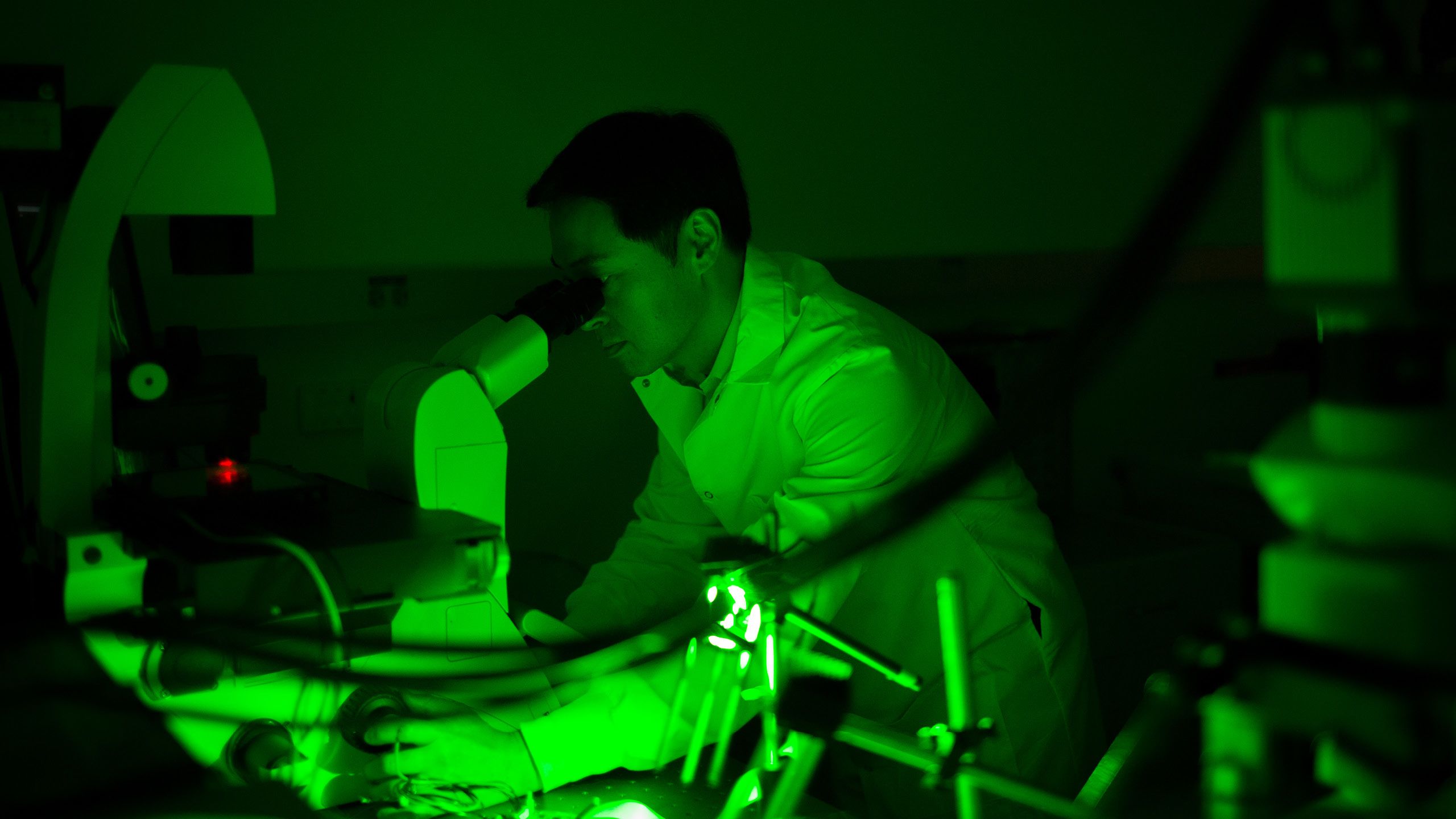 A man in a white coat looks into a microscope