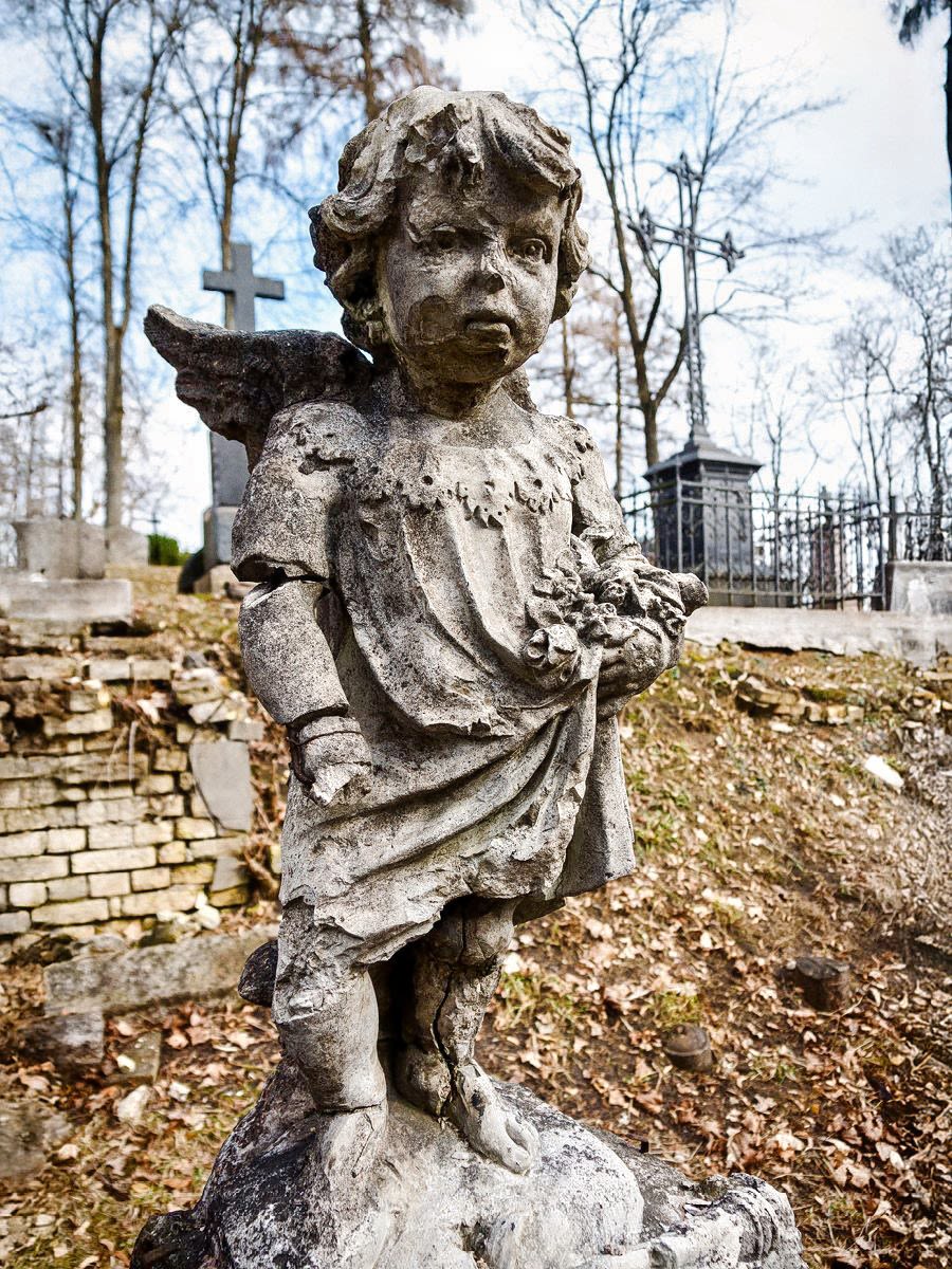 An old, weathered statue of a child angel over a grave.