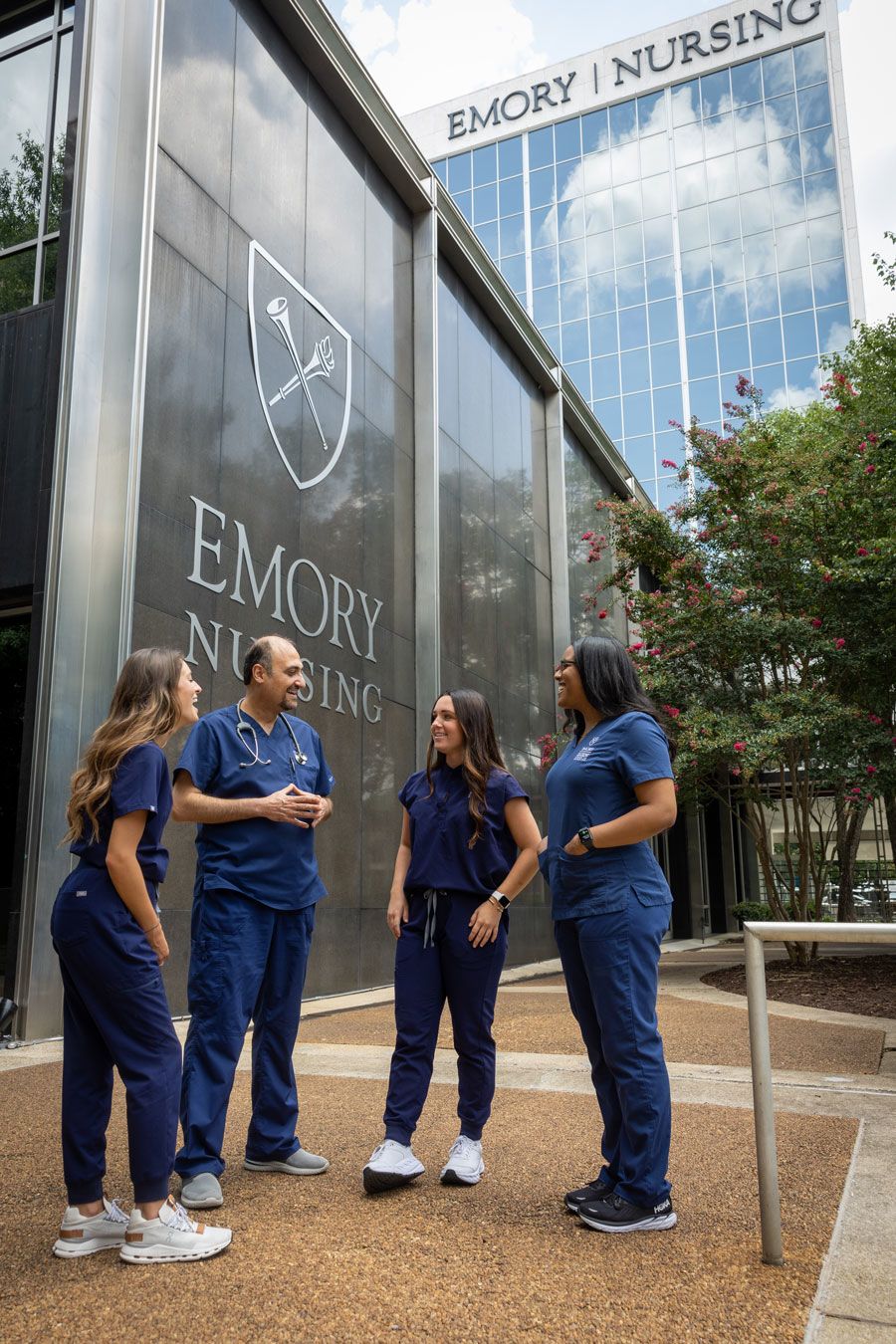 Three students and a professor stand outside the Emory Nursing Learning Center, a large building with a "Emory Nursing" sign on top.