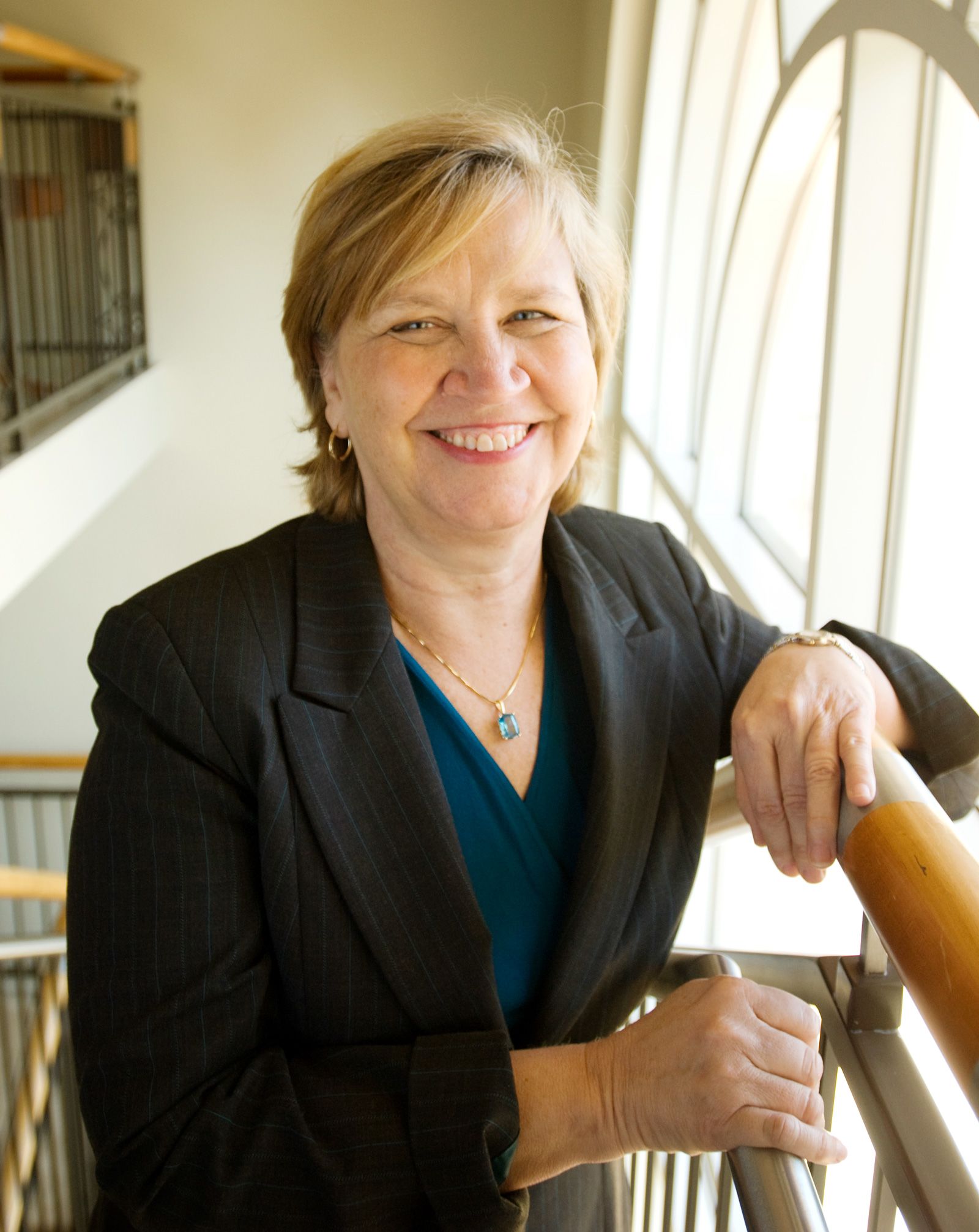 Portrait of Dean McCauley wearing a dark suit and with her arm on a banister