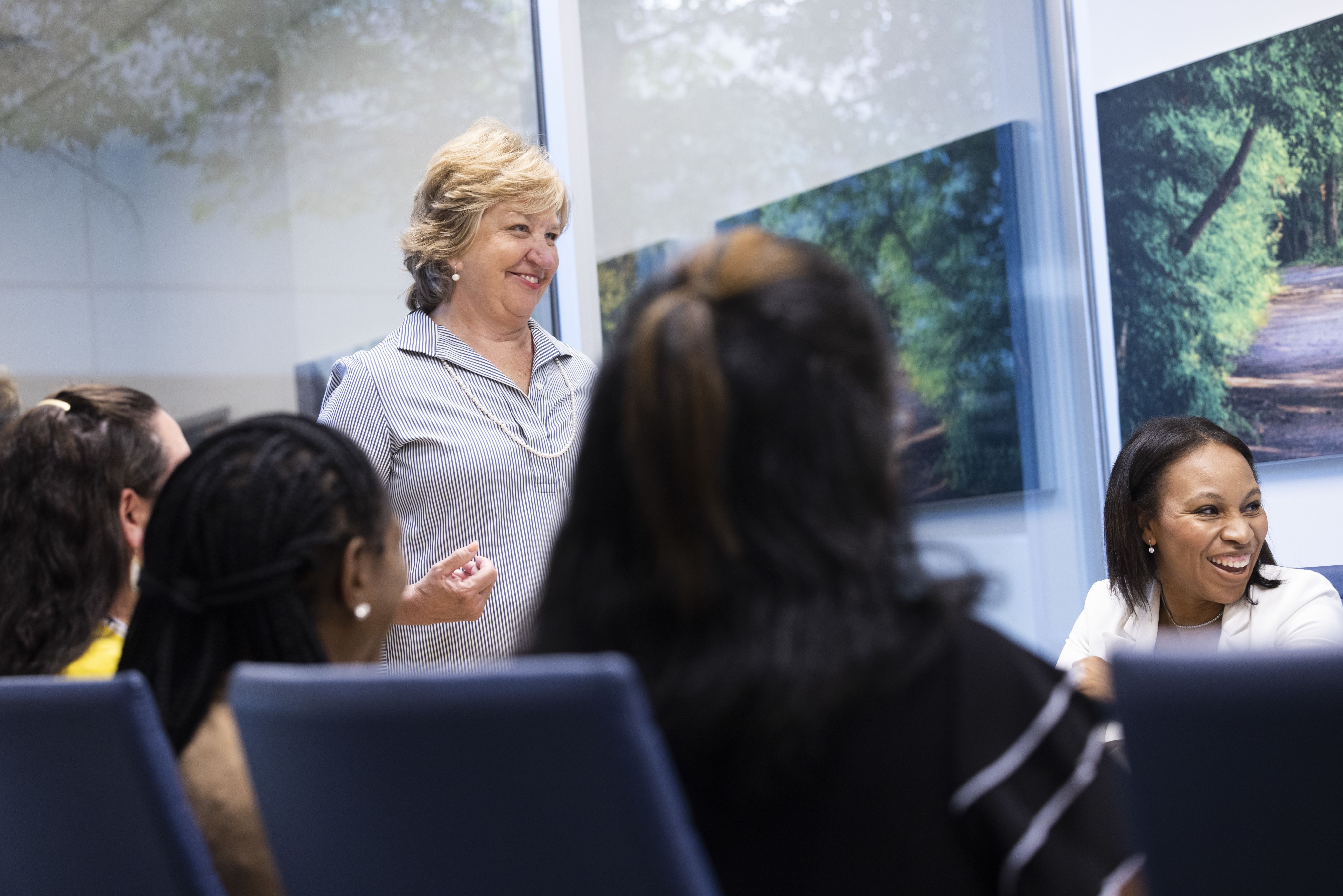 The dean standing at the head of the conference table with staff sitting around it. Image has a low angle and the dean is smiling widely.