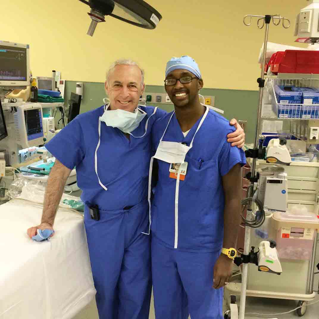 Dr. Andrew Reisner stands in an operating room with a younger man who was a former patient and is now a coworker at Children's Healthcare. 