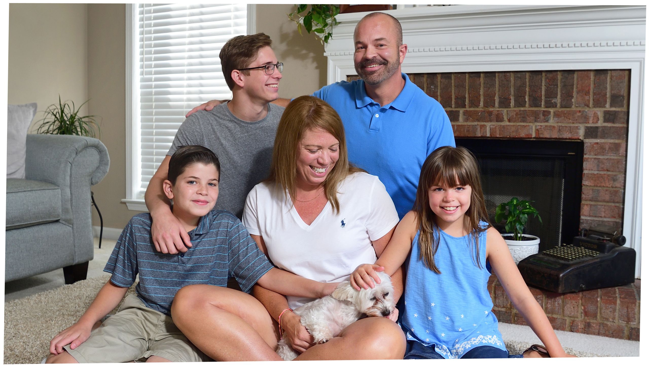 The Harrison family on the floor of their living room: in the back, kneeling, brother, Justin, with dad, Chris; front, sitting, Brayden, mom, Michelle, holding the family dog, Zoe, and sister, Jessica. 