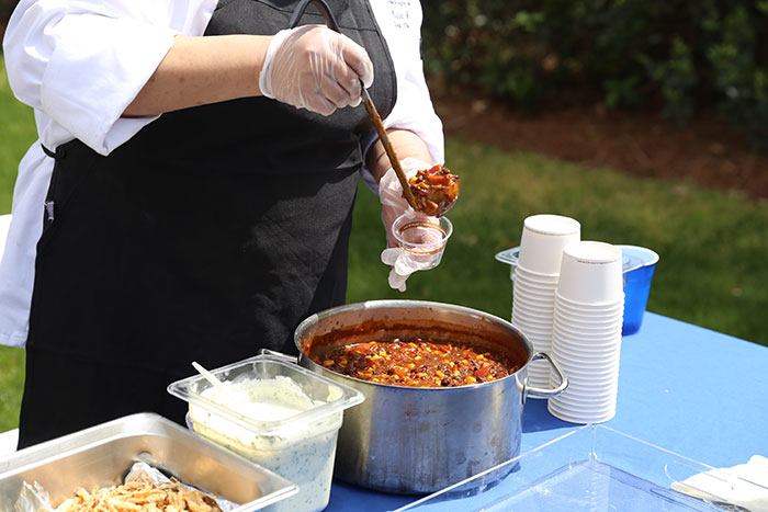 A chef from Emory Dining ladles out some chili in a plastic ramekin.