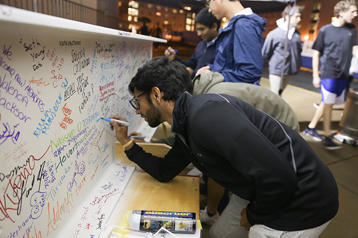 A student adds his name in light blue marker.