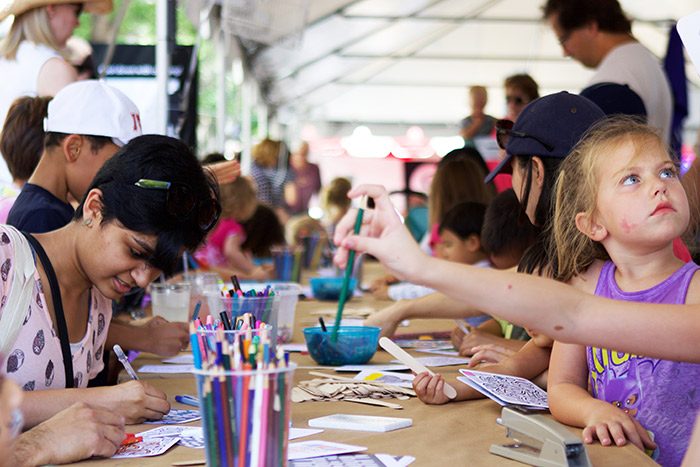 A group of adults and children sit and intently color at the Emory tent.