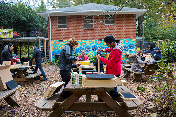 Several students work at picnic tables to build small screens to separate plants at the community gardens.