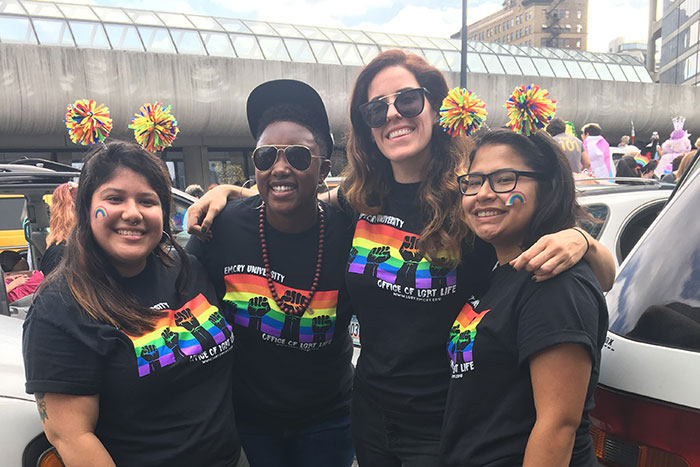 A group of four stand with their arms around each other in matching Emory LGBTQ pride t-shirts.
