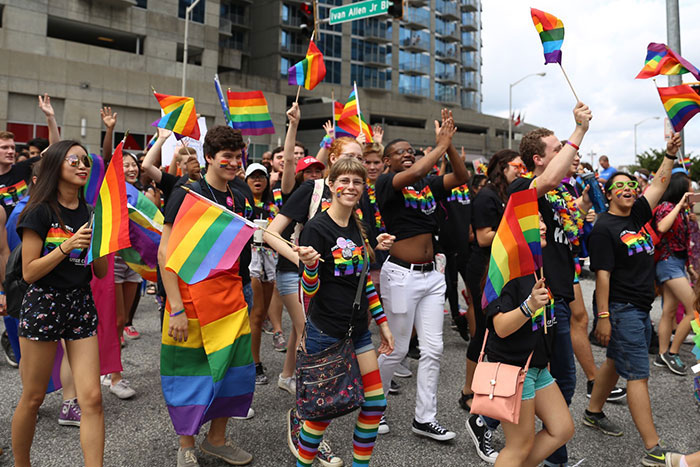 A crowd from Emory march in the 2017 Atlanta Pride Parade, waving rainbow flags.