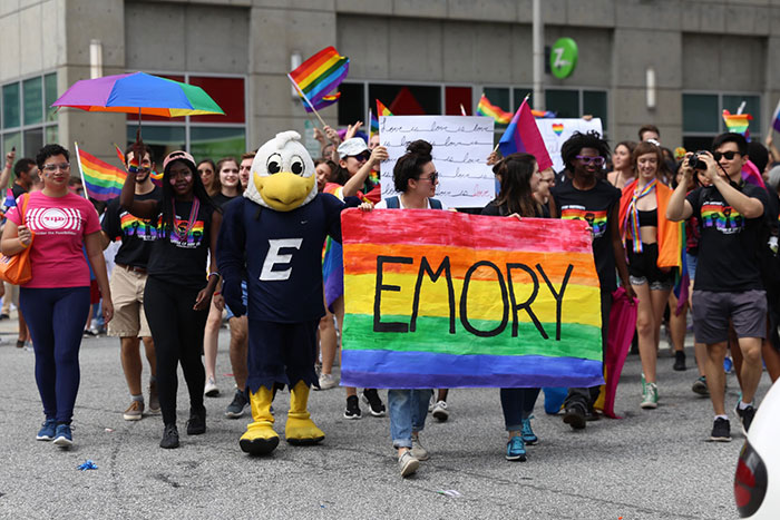 Several from the Emory community march in the parade while holding up homemade signs and wearing matching LGBTQ pride t-shirts.
