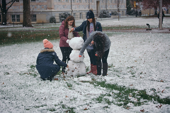 Four students use sticks and leaves to decorate a snowperson.