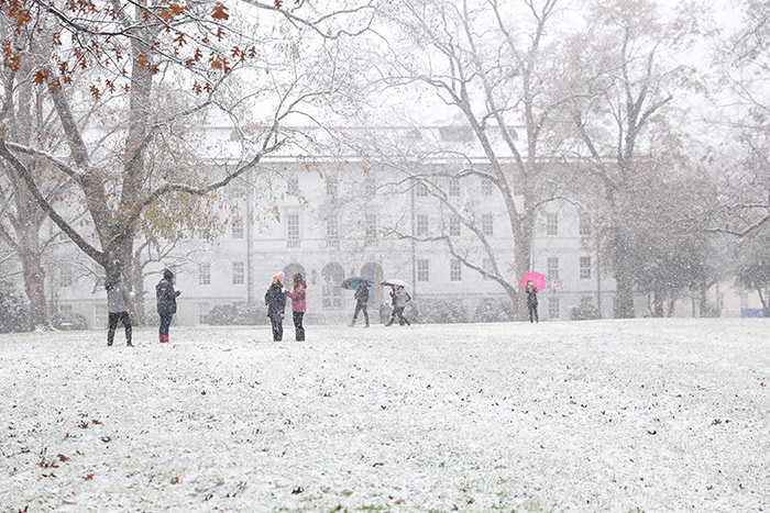 Half a dozen students walk through campus, some stopping to make snowballs.