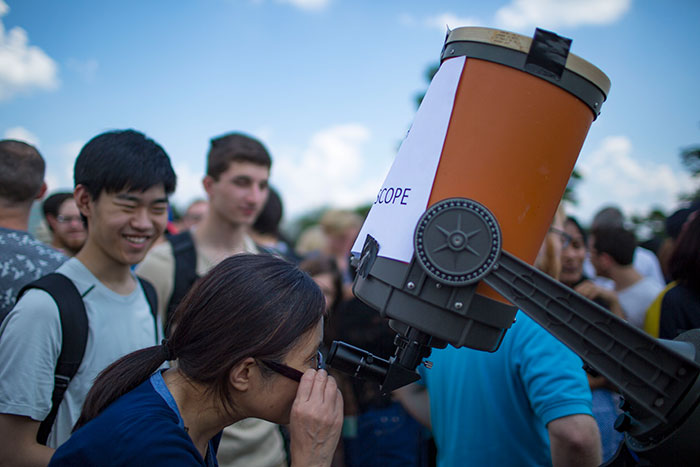 A student looks through a telescope at the eclipse above.