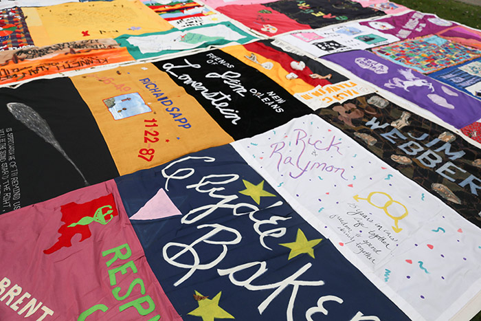 A close-up of a specific quilt shows the names of many sewn uniquely into the panels.
