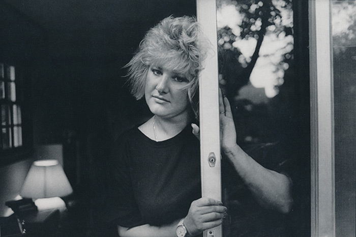 Photo from the exhibit of a woman named Deb, leaning on a sliding glass door.