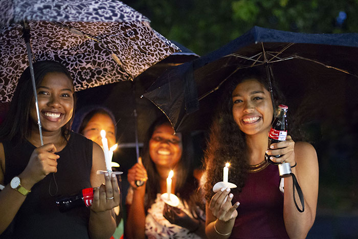 A group of students pose under shared umbrellas with their candles and Cokes