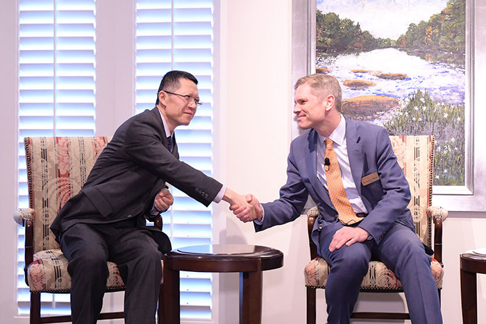 Emory College Dean Michael Elliott (right) shakes hands with Emory professor Tao Zha. Both are seated in large arm chairs with a small wooden table in between them.
