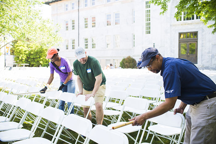 Three Emory employees measure the distance between rows of chairs with a stick and make adjustments